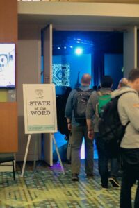 Attendees line up to go into a presentation near a "State of the Word" sign