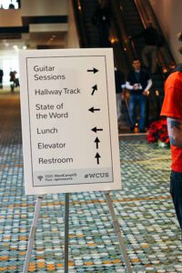 Large sign points to different sessions, event spaces, and restrooms.