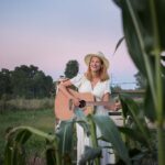 Tracy with her guitar in a cornfield at golden hour.