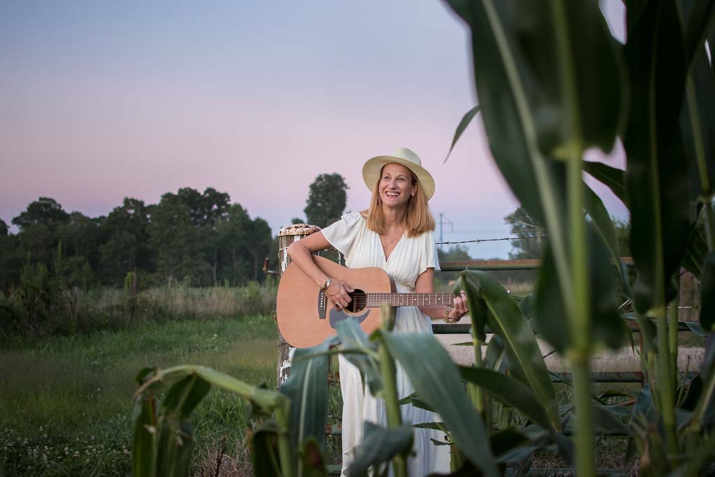 Tracy with her guitar in a cornfield at golden hour.