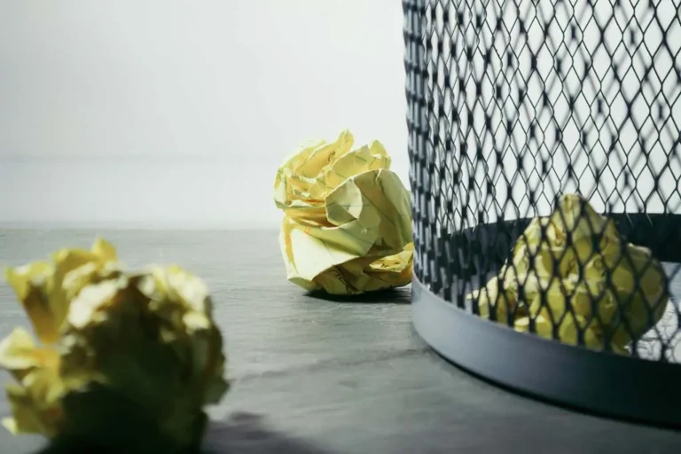 crumbled-up sheets of yellow paper on the floor by a metal wastebasket